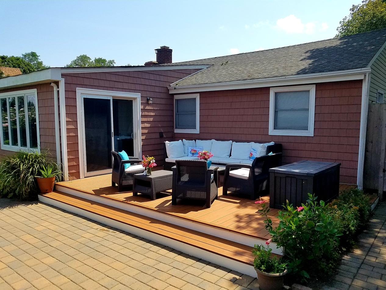 Cottage 1 deck with wicker seating, turquoise pillows, and fresh flowers against rose-shingled siding