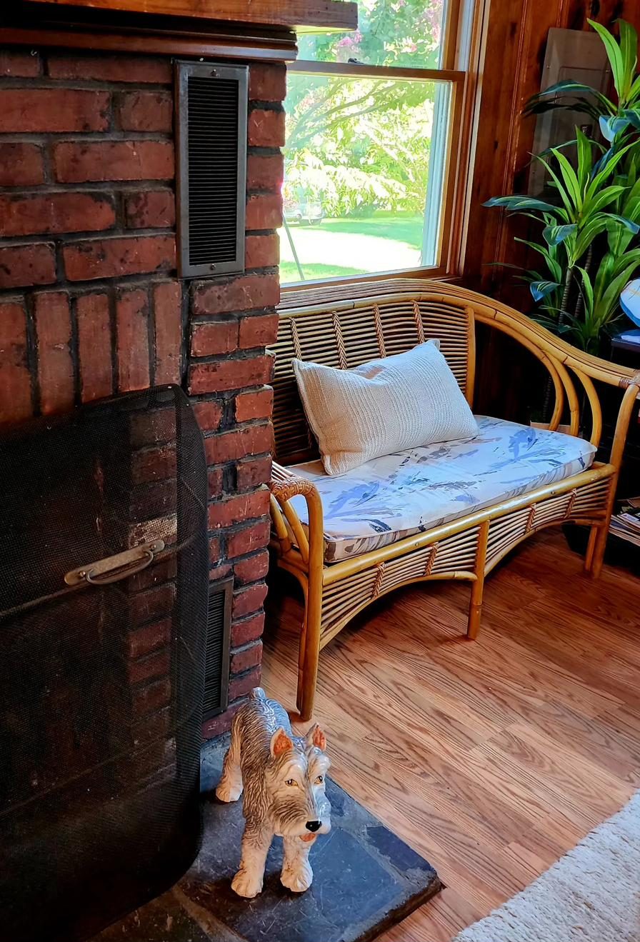 Brick wood-burning fireplace at Cottage 1 with a wicker bench and garden view