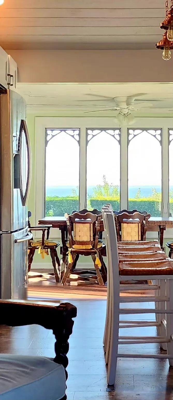 Dining sunroom at Cottage 1 with 1950s wood furniture, arched windows, bay views, and the galley kitchen visible alongside