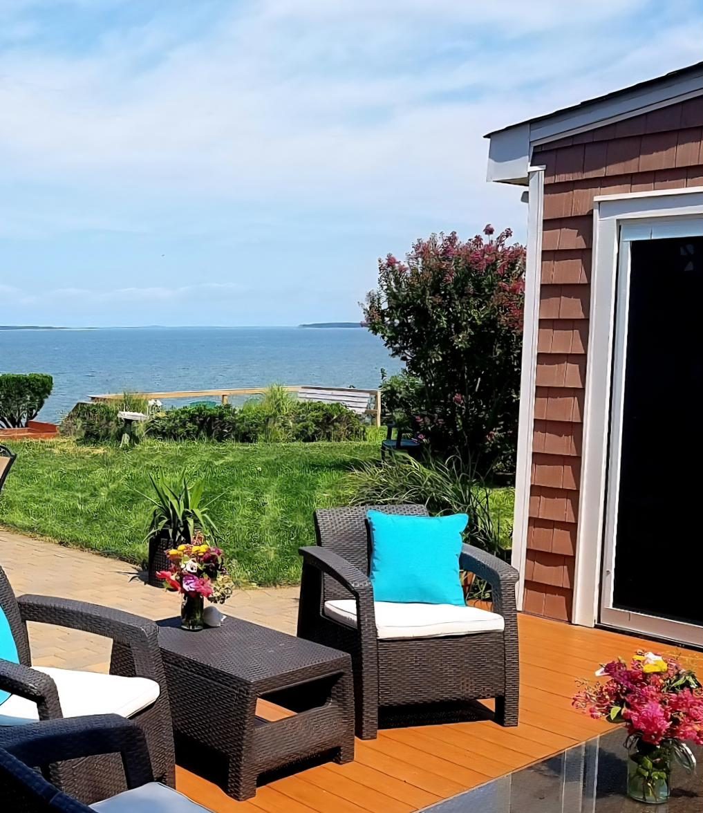 West deck at Cottage 1 with wicker seating and flowering crepe myrtle, overlooking the water