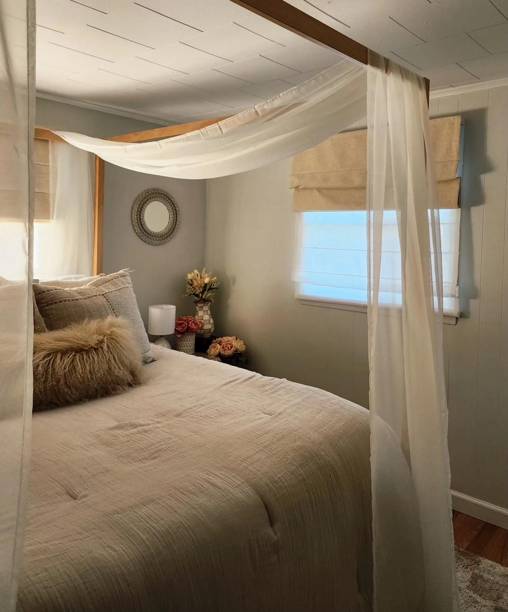 Canopy bedroom at Cottage 1 with soft draping and a round woven mirror