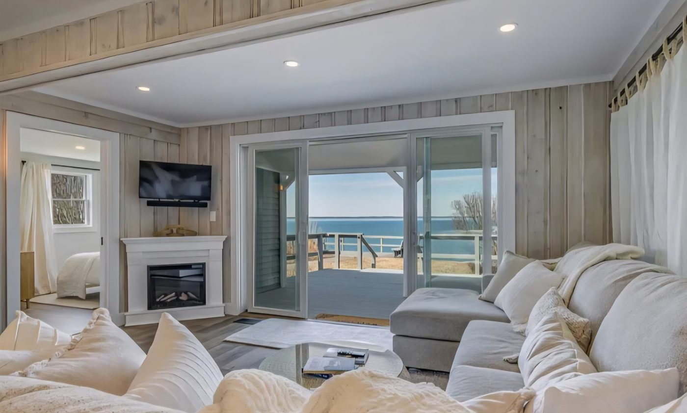 Living room at Cottage 2 with an electric fireplace, oversized chaise, and sliding glass doors open to the bay