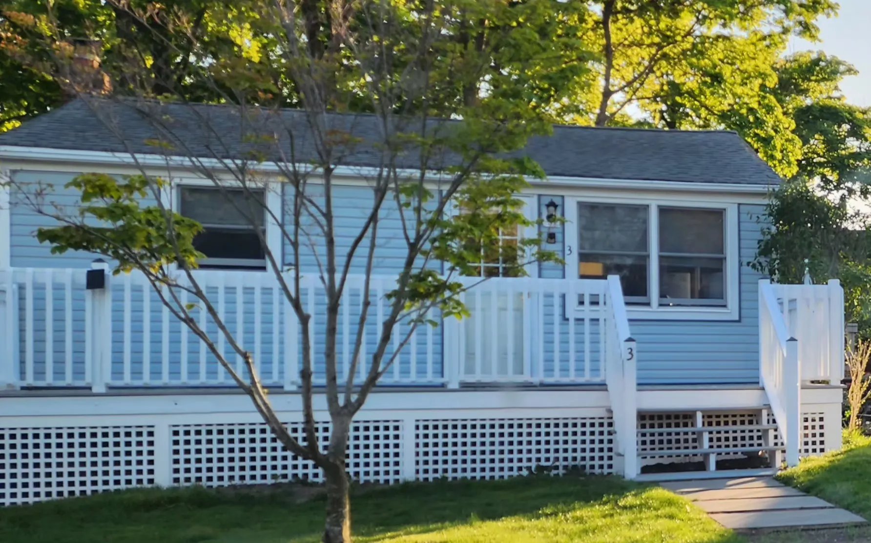 Full front facade of Cottage 3, sky-blue with white Victorian deck trim and lattice, house number 3 on the post