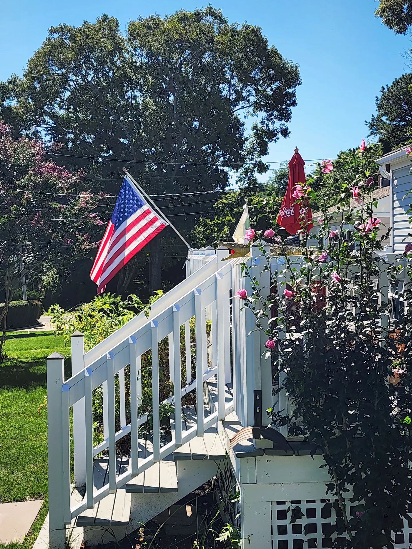 American flag and white Victorian deck railing at Cottage 3, framed by climbing roses