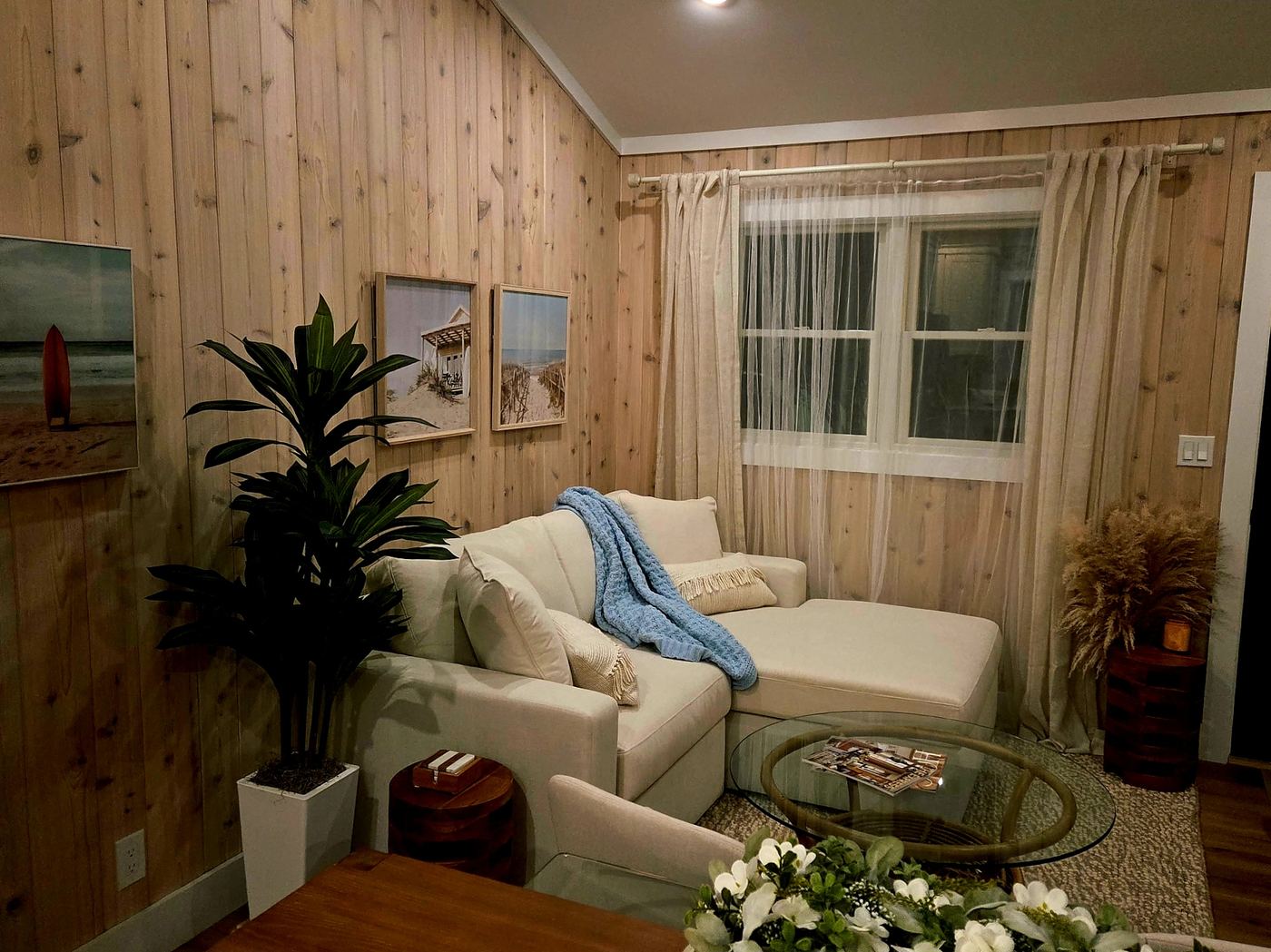 Cream sectional with a chaise arm, wood-paneled walls, and beach photography at Cottage 4