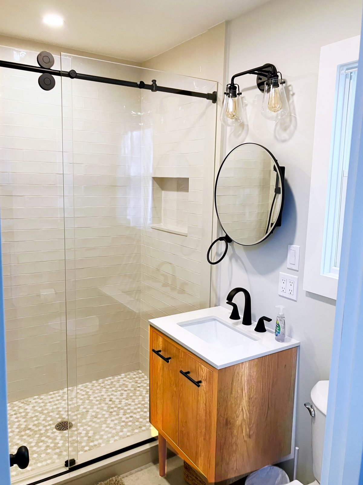 The Cottage 4 bathroom, with a subway-tile shower, matte black fixtures, a round mirror, and a honey-toned wood vanity