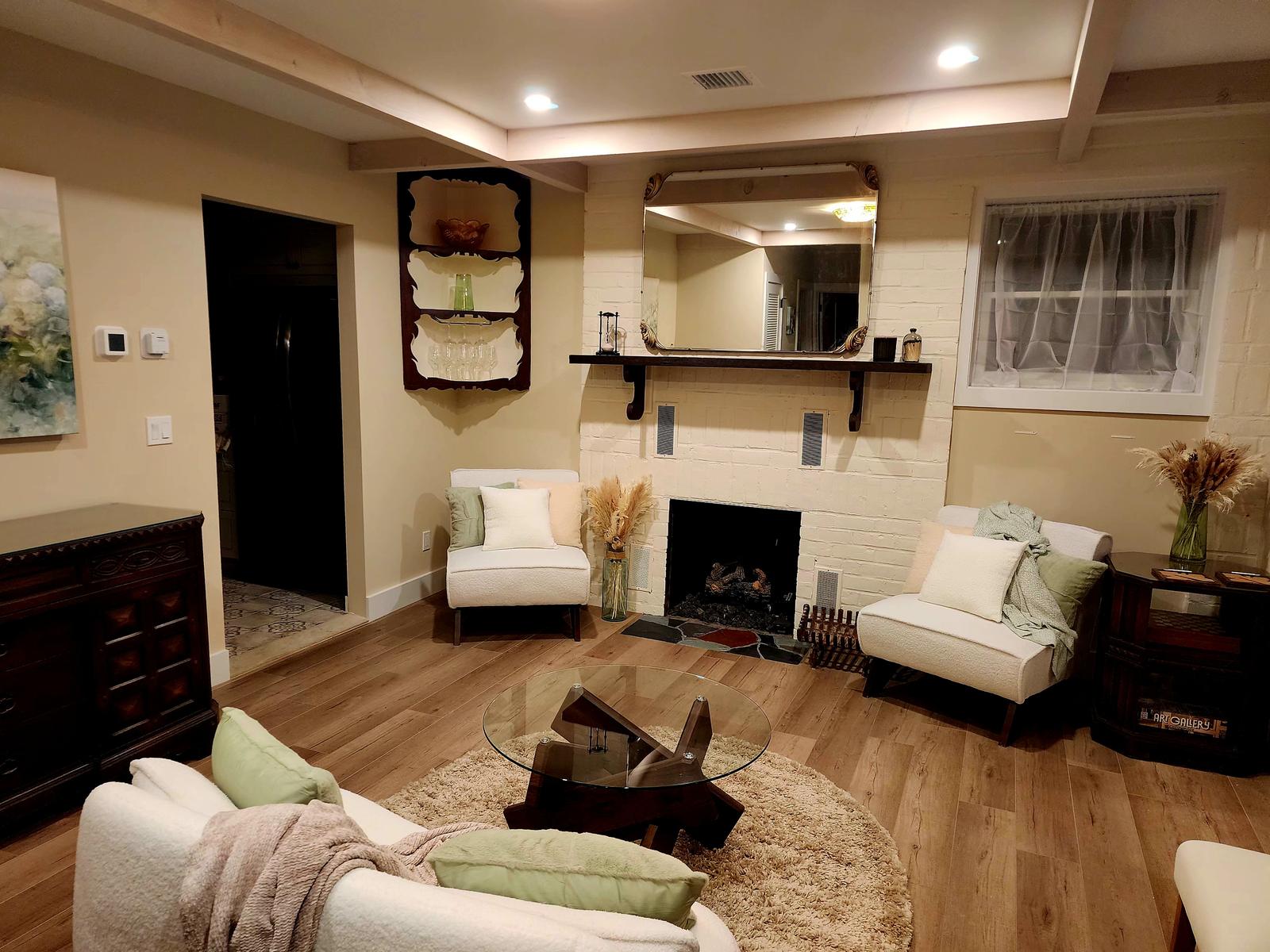 The fireplace room, with a wall-mounted glassware bar, dark antique dresser, and boucle loveseat