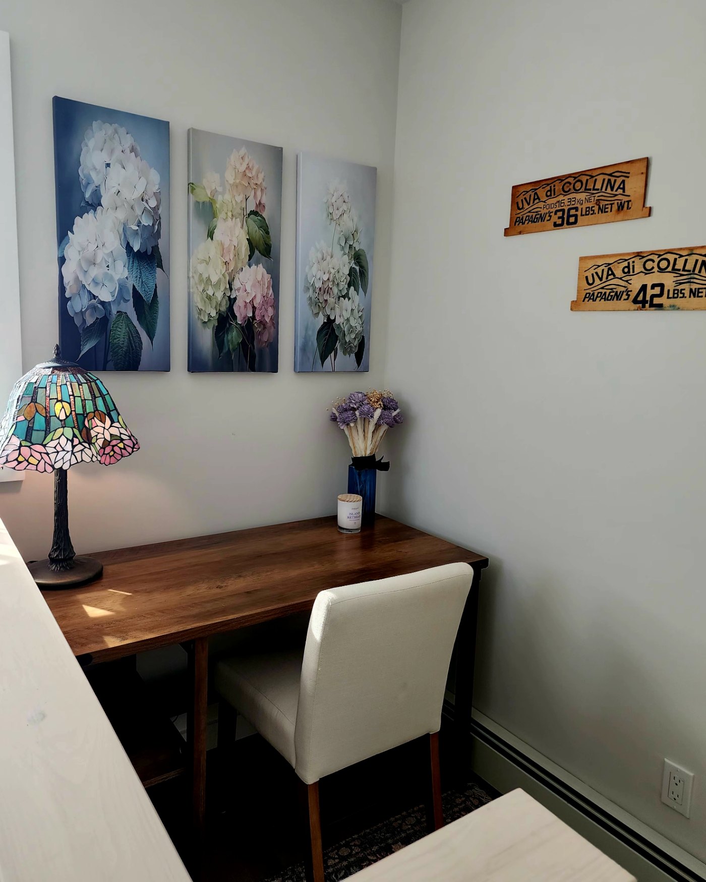 The home office, with a wood desk, stained-glass lamp, and hydrangea triptych