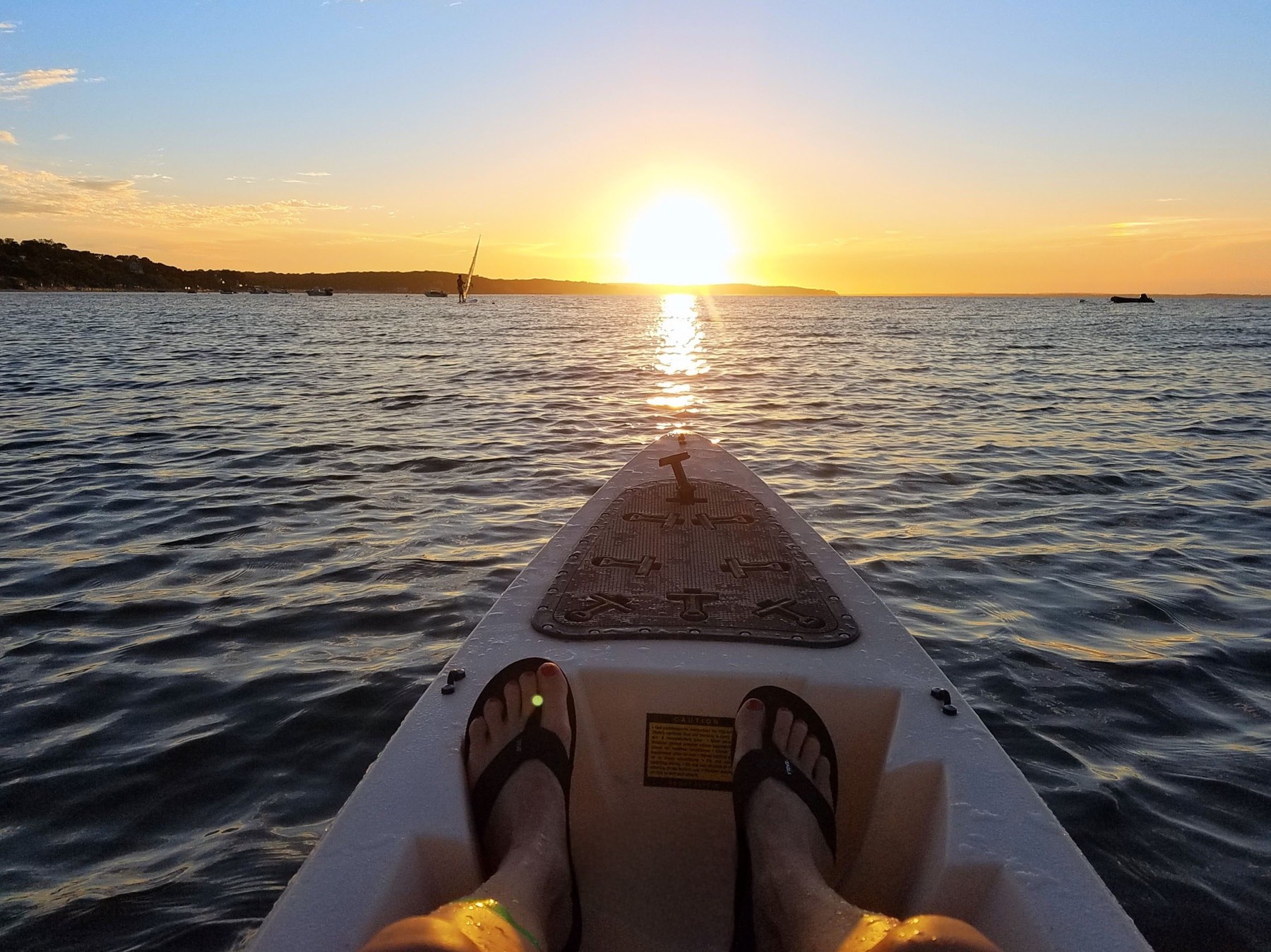 View from the bow of a kayak toward the sunset over Peconic Bay, with a windsurfer in the distance