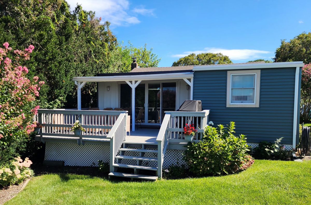 Cottage 2, The Captain's House exterior, blue-gray cottage with covered porch, deck, and flowering shrubs