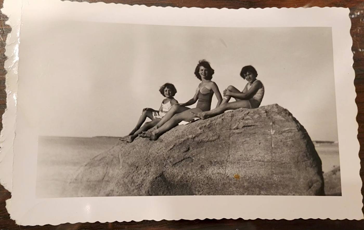 Three girls sitting on a large rock at the beach, vintage photograph