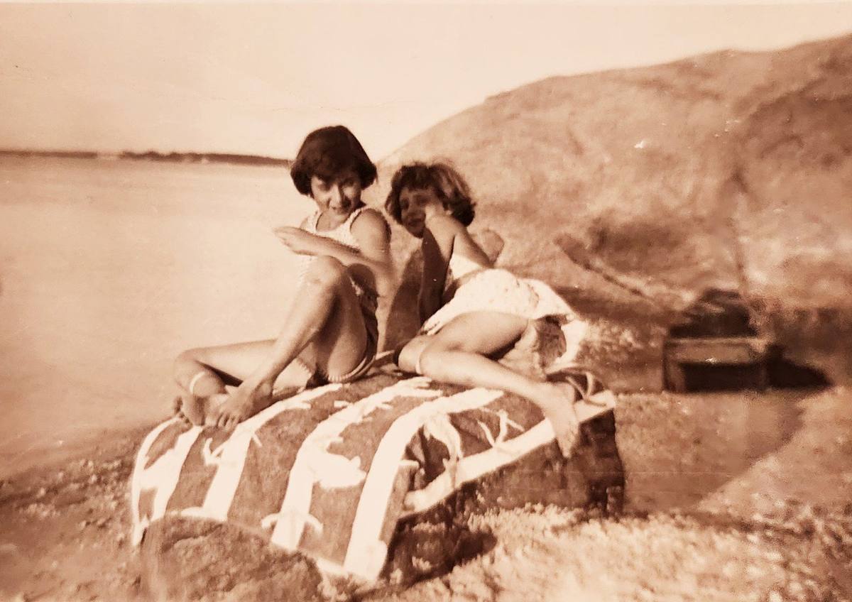 Two girls sitting on a smaller rock at the shoreline, vintage photograph