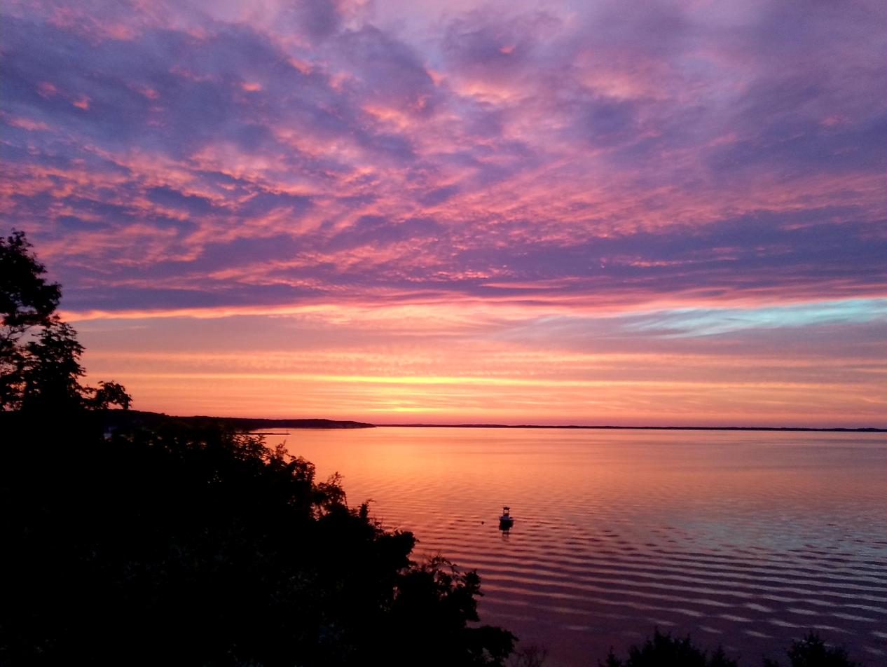 Pink and violet clouds over Peconic Bay at sunset, with a boat on the water