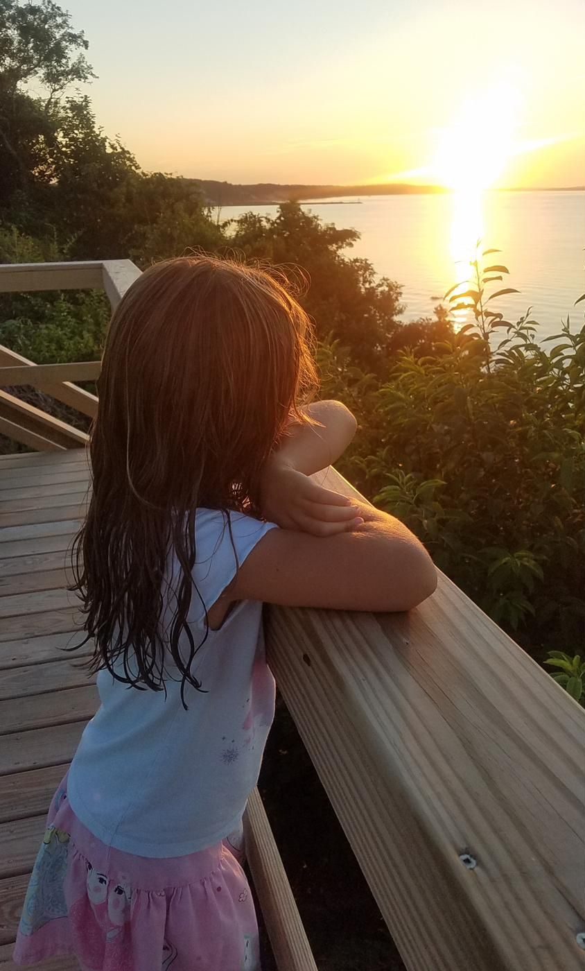 A child watching the sunset from the deck railing