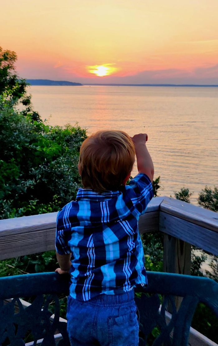 A young boy watching the sunset from a bench on the deck