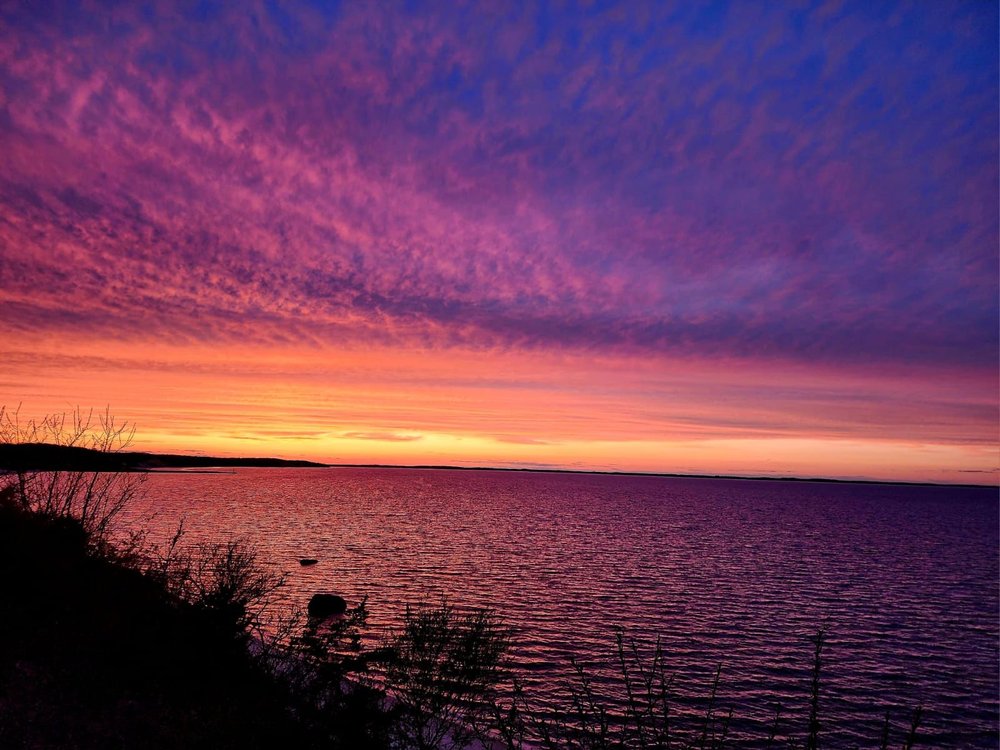 Deep violet and orange sunset sky reflected across the bay