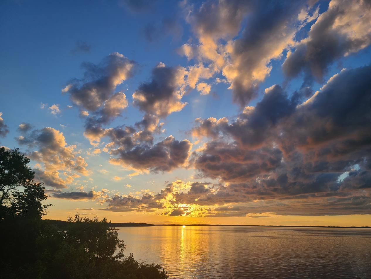 Sun setting through scattered clouds over calm water