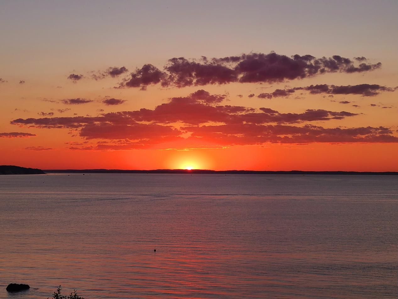 The sun setting into a band of clouds over the bay