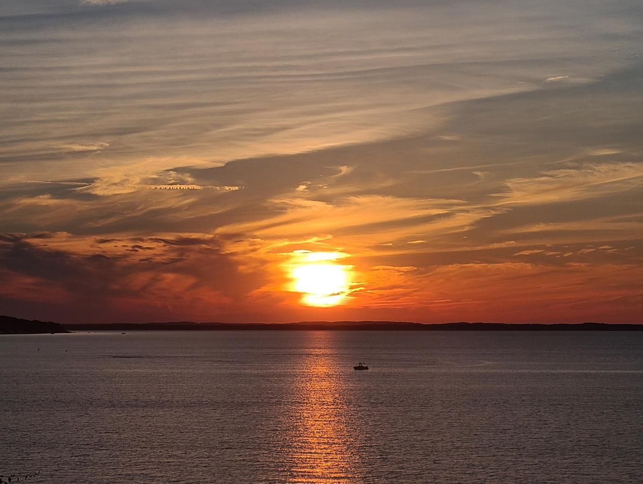 Sun breaking through wispy clouds with a boat silhouetted below