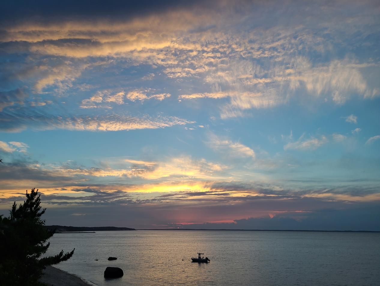 Wispy golden clouds at sunset with a boat on the water