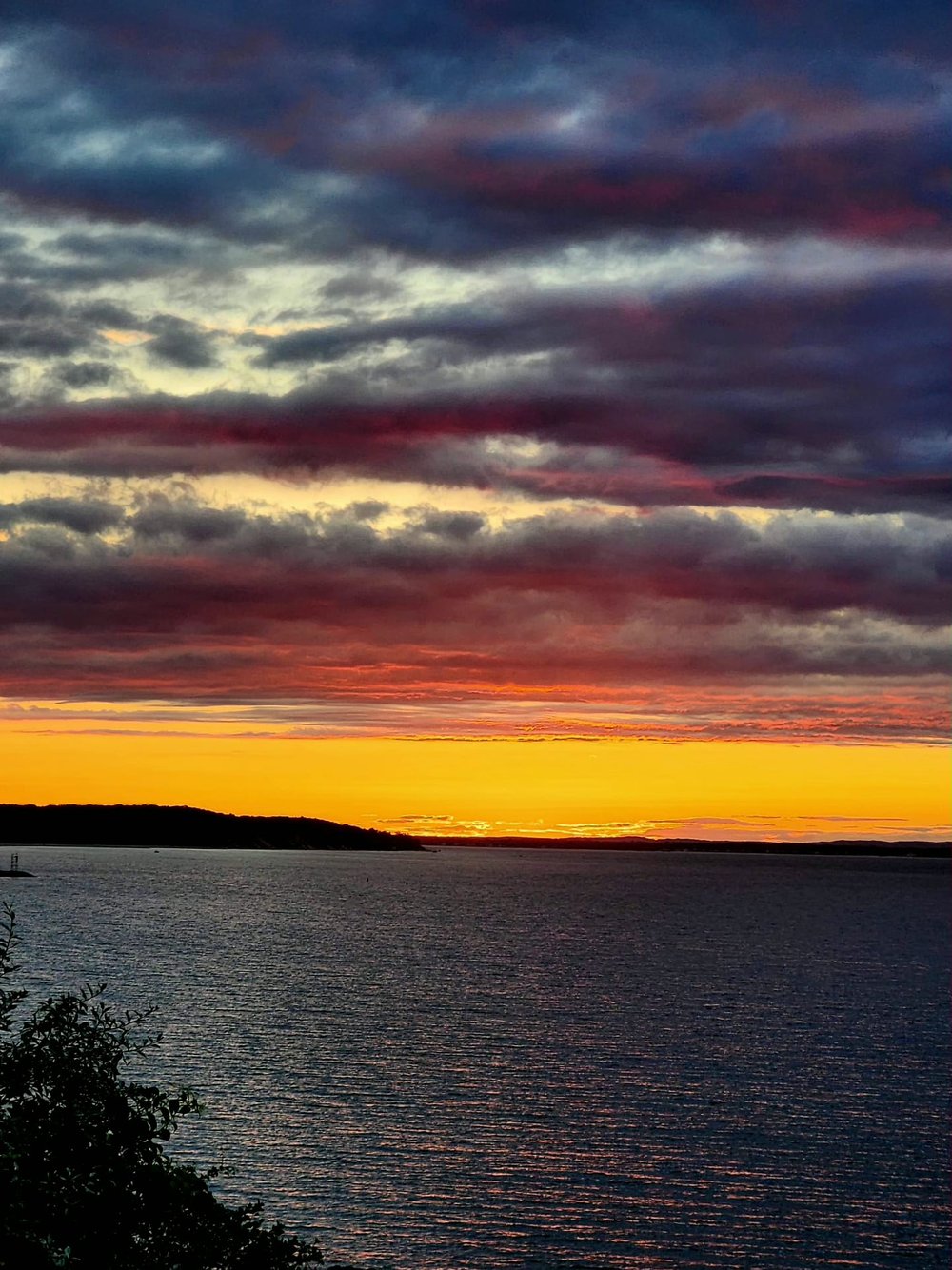 Layered pink and violet storm clouds over the bay with a golden horizon