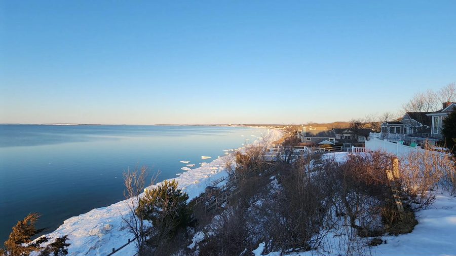 Winter view along the snowy bluff with ice on the bay and cottages beyond