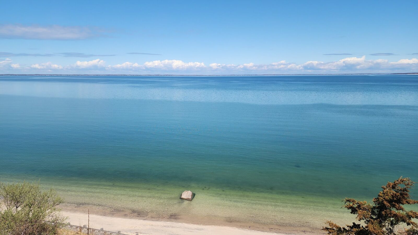 The sandy beach below the bluff, with clear blue-green water stretching out across the bay